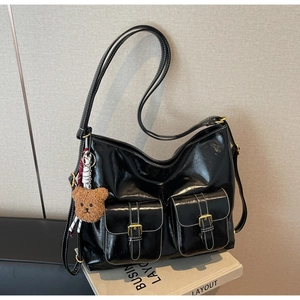 Détail du sac à bandoulière noir brillant avec surpiqûres blanches et breloque ours