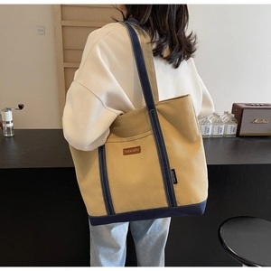 Canvas tote bag with khaki body and navy blue straps shown from a back view on a model