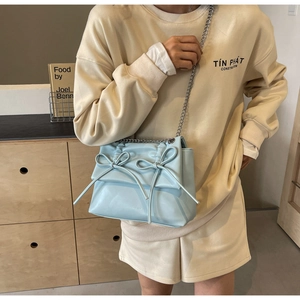 Detail of light blue crossbody bag featuring pleated bow design and silver metal chain strap