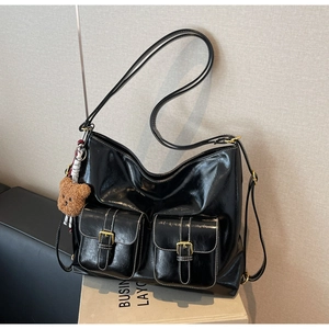 Détail d'un sac en cuir noir brillant avec poches avant et charm d'ours peluche