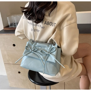 Detail of light blue PU leather shoulder bag with decorative bows and silver chain strap