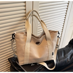 Detail of beige canvas tote bag showing dark leather patch and adjustable strap