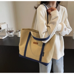 Close-up of a large beige and navy blue canvas tote bag worn by a model in a cafe