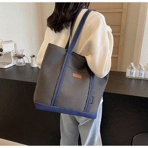 Detailed side view of large canvas tote bag with contrast blue straps and logo patch