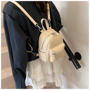 Detailed view of mini woven backpack in beige with silver zippers worn on stairs