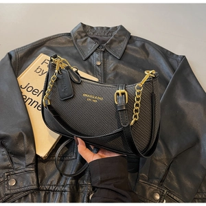 Detail of black textured crossbody bag with gold hardware and logo on leather jacket