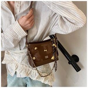 Detailed shot of brown leather crossbody bag with gold metal charms on striped shirt model