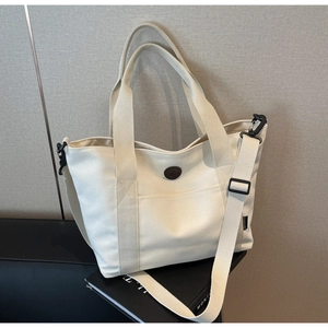 Close-up of cream canvas tote bag with brown leather logo and adjustable strap details