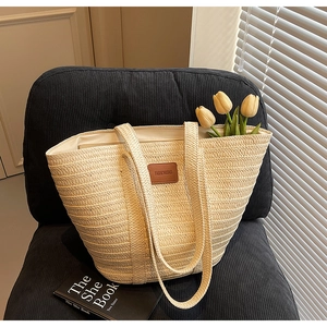 Close-up of woven straw tote bag featuring a brown leather label and stylish thin straps
