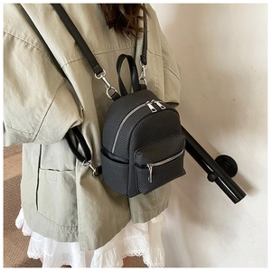 Detail of a mini black quilted backpack with silver zippers on a fashion model