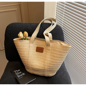 Detail of handwoven beige straw tote bag with brown leather patch on a textured chair