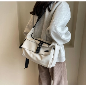 Detailopname van een witte minimalistische nylon schoudertas met zwarte riem en label