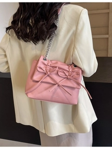 Pink crossbody bag with chain strap and bow detail worn with a beige blazer jacket