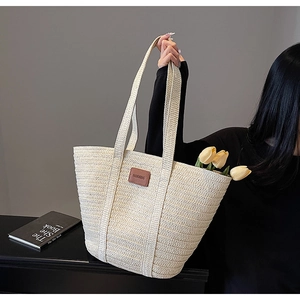 Detail of off-white woven straw tote bag with brown leather patch and long handles