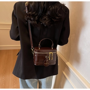 Details einer dunkelbraunen Lackleder-Boxtasche mit goldenen Beschlägen am Modell