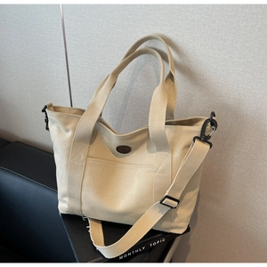 Detail of off-white canvas tote bag featuring brown logo patch and detachable shoulder strap