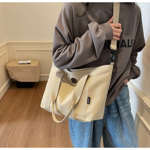 Detail of beige canvas tote bag showing front pocket and detachable woven shoulder strap