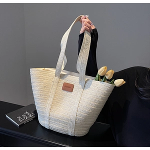 Detail of hand-woven beige straw tote bag with brown leather logo and yellow tulips
