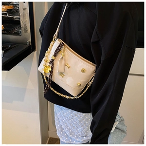 Close-up of beige crossbody bag with gold bone ornaments and metallic chain strap