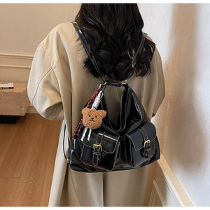 Détail d'un sac à dos hobo en cuir noir avec surpiqûres blanches et pendentif ours