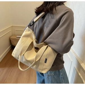 Detail view of a large beige canvas tote bag worn by a model in a modern home setting