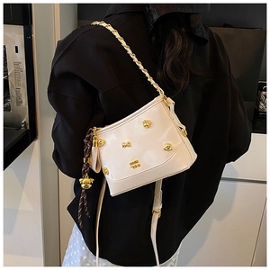 Detail of white glossy crescent bag with gold paw rivets and woven charm on model