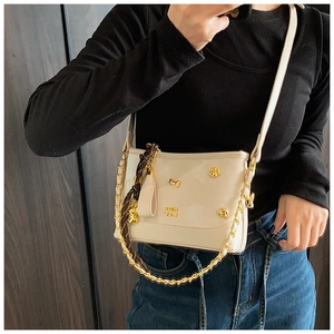 Detail of off-white tote bag with gold charms, chain strap, and geometric pattern scarf