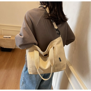 Detail of beige canvas tote bag showing black adjustable strap and metal hardware buckle