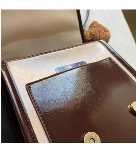 Dettaglio cartella vintage in pelle bicolore con tasca frontale e ciondolo orsetto morbido
