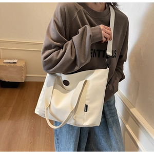 Detail of white canvas tote bag with front pocket, top handles and adjustable shoulder strap