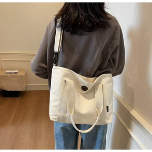 Detail of off-white canvas tote bag featuring decorative badge and adjustable strap