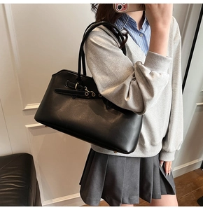 On-shoulder view of a large black vintage shell-shaped tote bag with gold buckle hardware