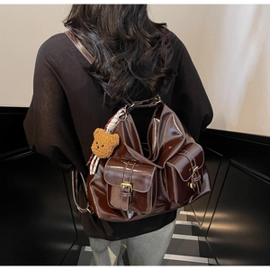 Détail du sac à bandoulière marron brillant avec doubles poches et breloque ours peluche