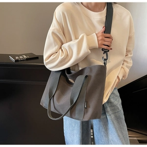 Detailed view of grey canvas tote bag with adjustable black nylon strap on model