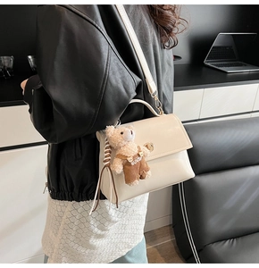 Close-up of beige crossbody bag with gold twist lock and cute plush bear charm accessory