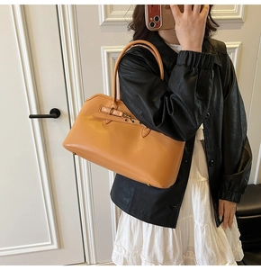 Detail of tan vintage tote bag featuring decorative straps and gold metal feet on bottom