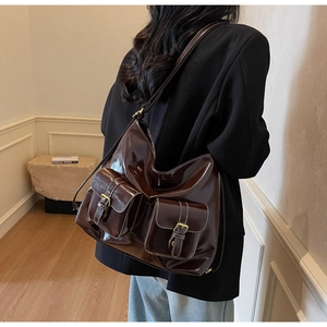 Détail d'un grand sac hobo en cuir verni marron avec surpiqûres blanches et boucles dorées