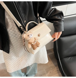 Detalle de bolso de cuero blanco crema con cierre dorado y colgante de oso de peluche