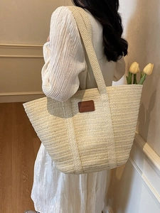 Stylish large straw tote bag in beige with brown leather patch on a model shoulder