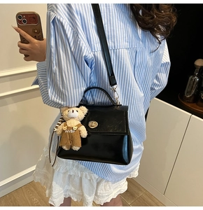 Detail of black patent leather crossbody bag featuring a cute teddy bear plush charm
