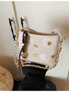 Cream white glossy tote bag with gold metal charms and woven chain strap held by a person