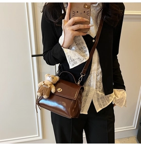 Detail of vintage dark brown faux leather crossbody bag with teddy bear pendant accessory