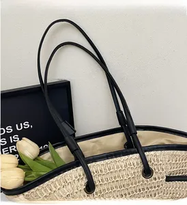 Close-up of woven straw tote bag with black leather handles and reinforced edging