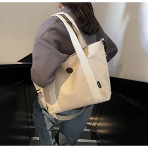 Detail view of large cream canvas tote bag with wide shoulder strap and circular patch