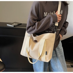Close-up of cream canvas tote bag with adjustable strap and brown circular logo detail