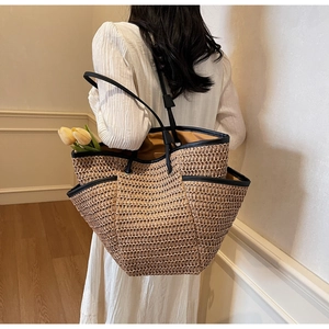Detail of large straw woven tote bag featuring black leather handles and practical side pockets