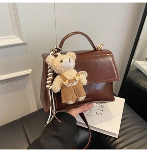 Detalle de bolso marrón en piel PU con cierre dorado y colgante de osito de peluche