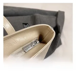 Détail de la fermeture éclair argentée et tirette gravée sur le cabas en cuir plissé beige