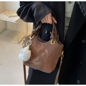 Detailansicht der dunkelbraunen glänzenden Beuteltasche mit weißem Plüsch-Bommel-Anhänger