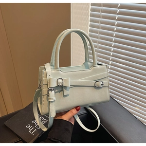 Detail of mint green square handbag with top handle, bow decor and adjustable strap